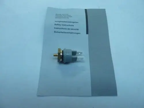 Temperatursensor von Remeha auf einem Blatt Papier mit Sicherheitshinweisen. Der Sensor hat zwei Anschlussstifte und eine metallische Befestigung.